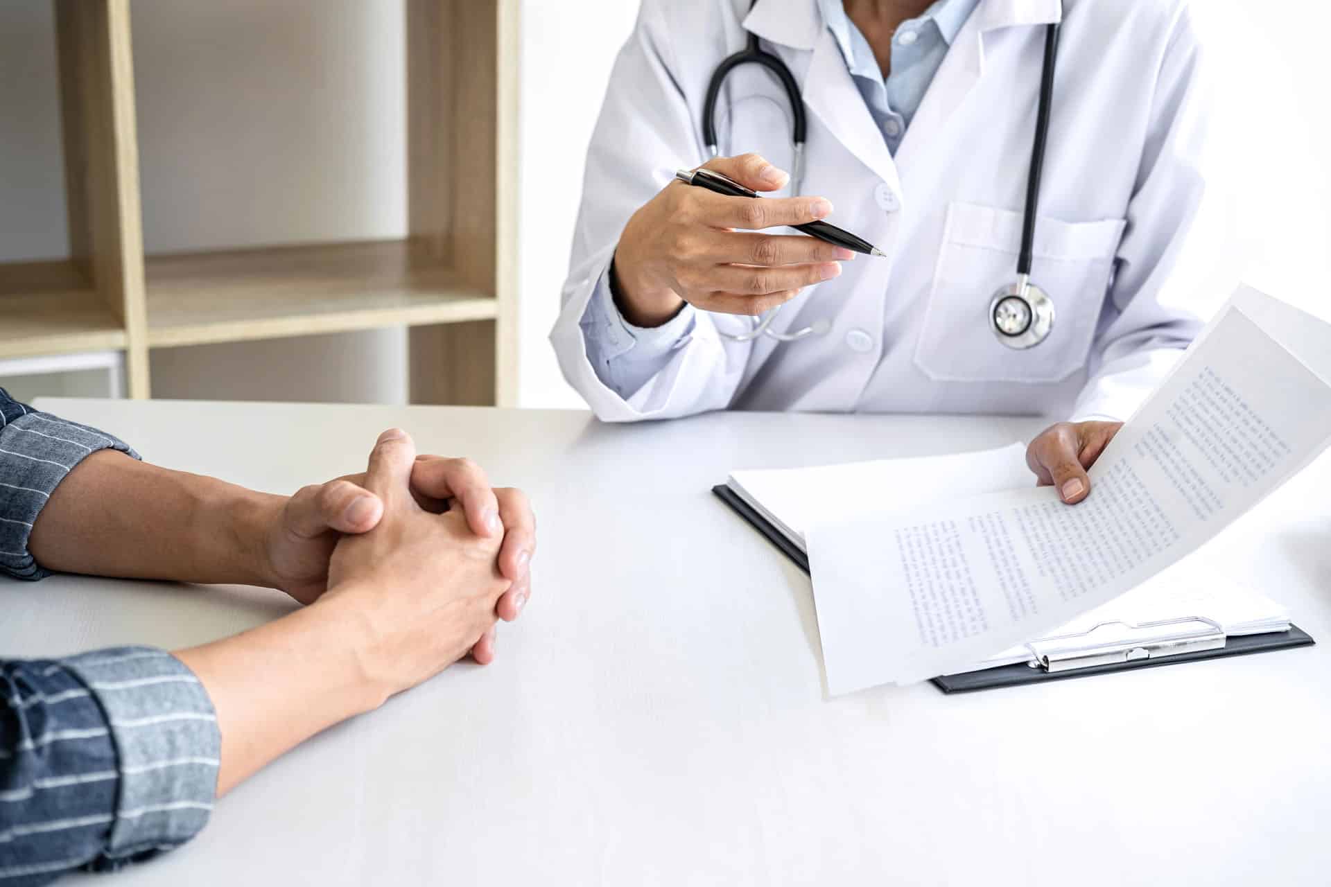 Doctor with stethoscope holding paper presenting it to person sitting next to them