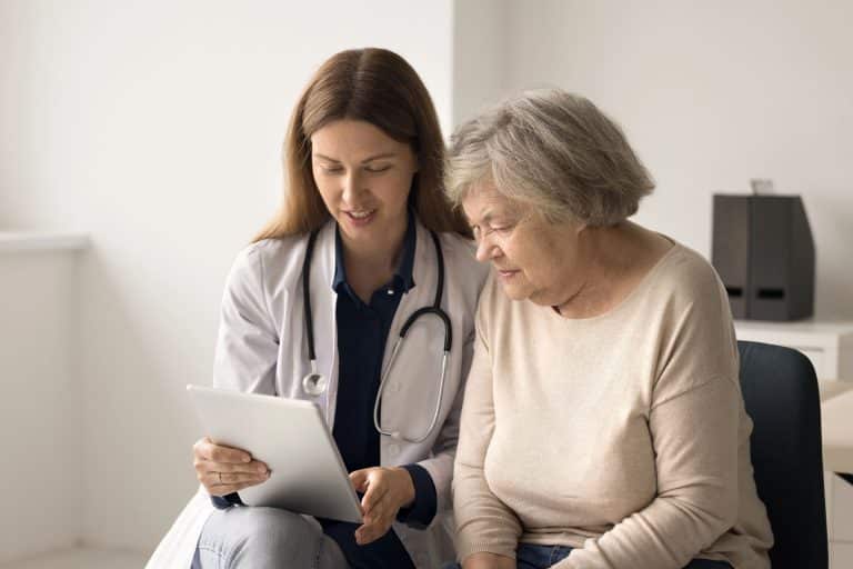 Doctor with stethoscope sat talking to old person looking at chart