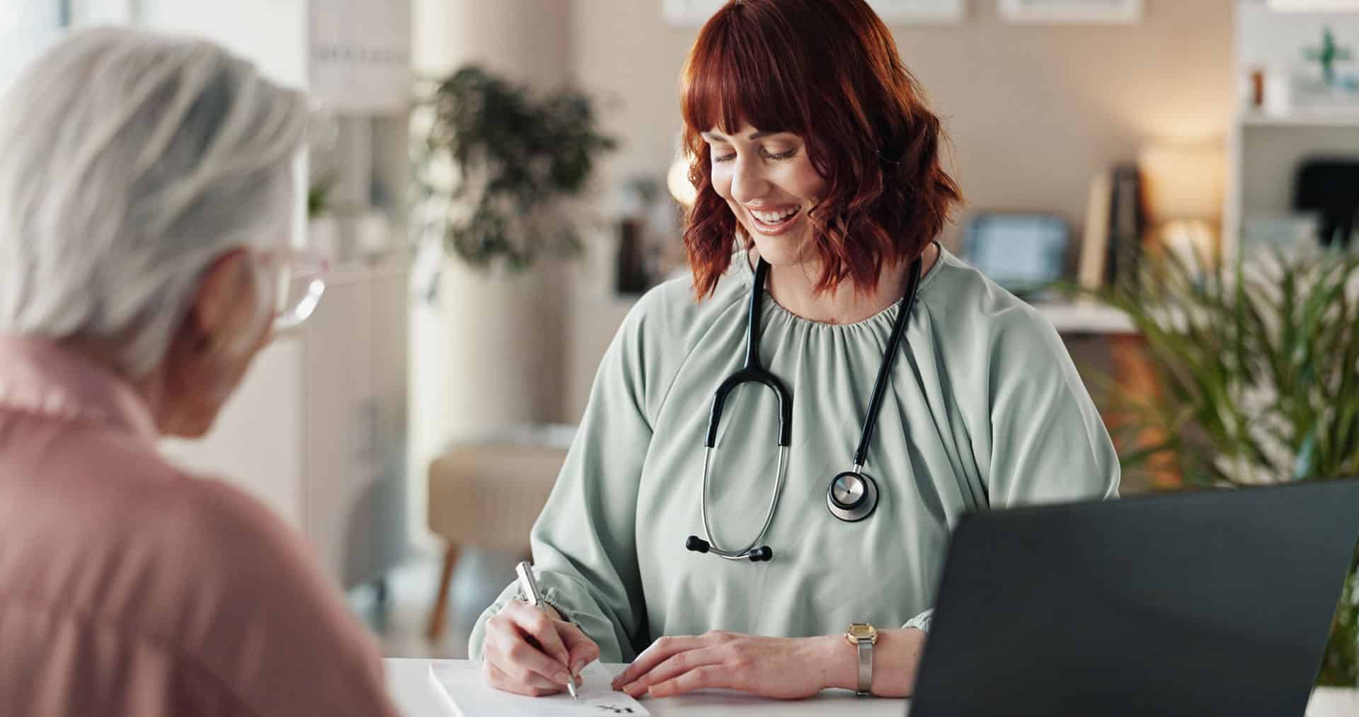 Doctor with stethoscope sat across the desk from old person